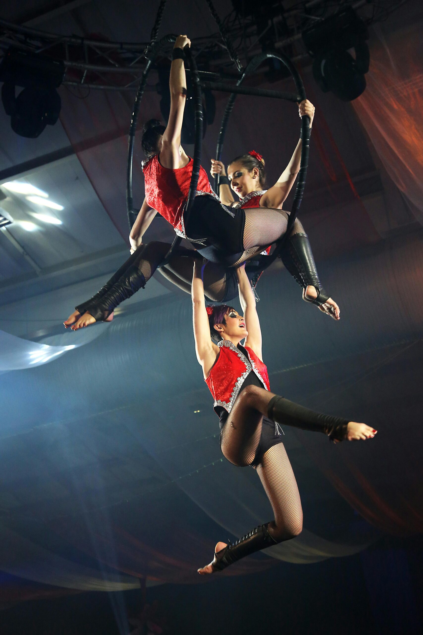 Three female performers execute stunning aerial acrobatics on stage at a vibrant indoor event.